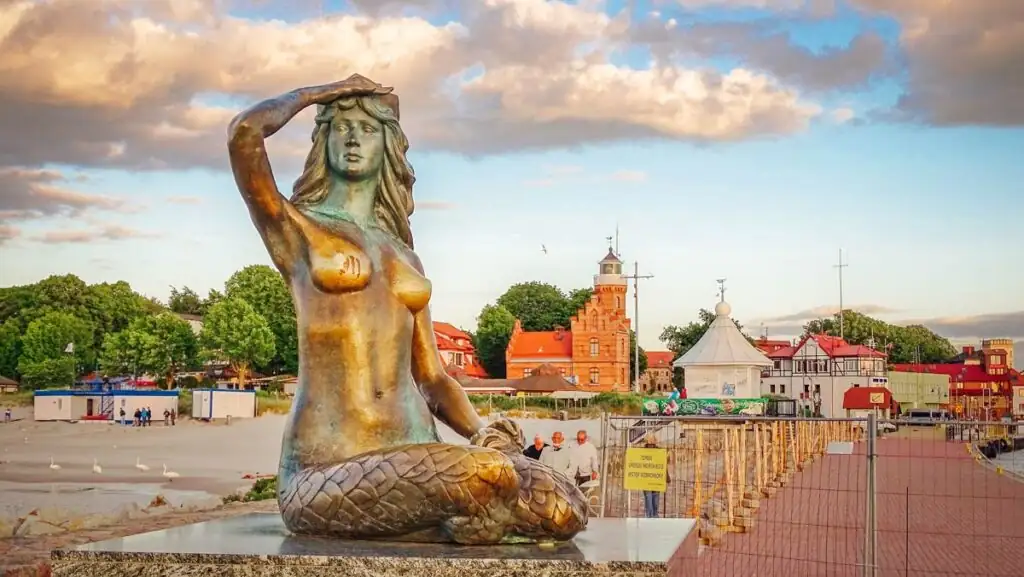 Die Bronzestatue der Meerjungfrau „Syrenka“ sitzt am Ende der östlichen Hafenmole von Ustka und blickt auf die Ostsee hinaus. Die Skulptur, ein Wahrzeichen der Stadt, steht auf einer kleinen Plattform und symbolisiert die enge Verbindung Ustkas mit dem Meer.