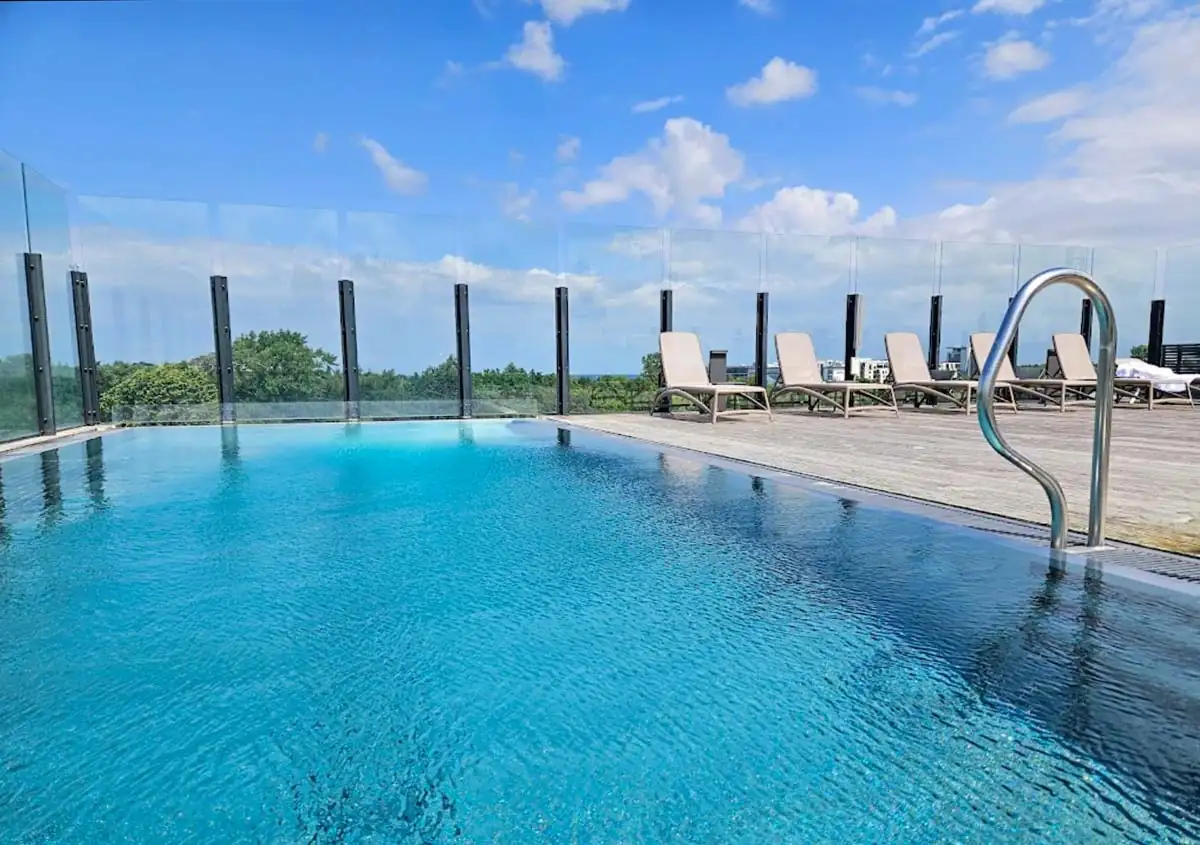 Infinity Pool auf dem Dach des Hotels umgeben von moderner Liegefläche und Blick auf die umliegende Natur.