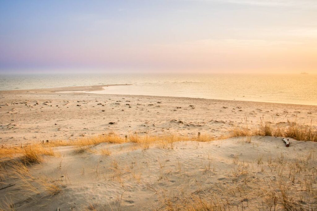 Ein farbenprächtiger Sonnenuntergang am Strand von Hel, bei dem die Sonne in warmen Orangetönen über der Ostsee versinkt. Der Himmel leuchtet in einem beeindruckenden Spektrum aus Rot, Pink und Lila, während die sanften Wellen des Meeres den letzten Schimmer des Tageslichts reflektieren. Ein stimmungsvoller und friedlicher Moment in der Natur.