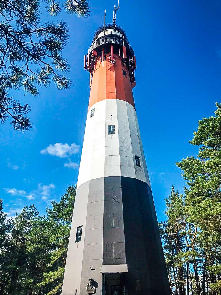 Der rot-weiß-schwarze Leuchtturm Stilo bei Łeba erhebt sich majestätisch auf einem bewaldeten Hügel. Mit seiner schlanken Struktur aus Stahl und Beton bietet er einen markanten Kontrast zur umgebenden Natur.