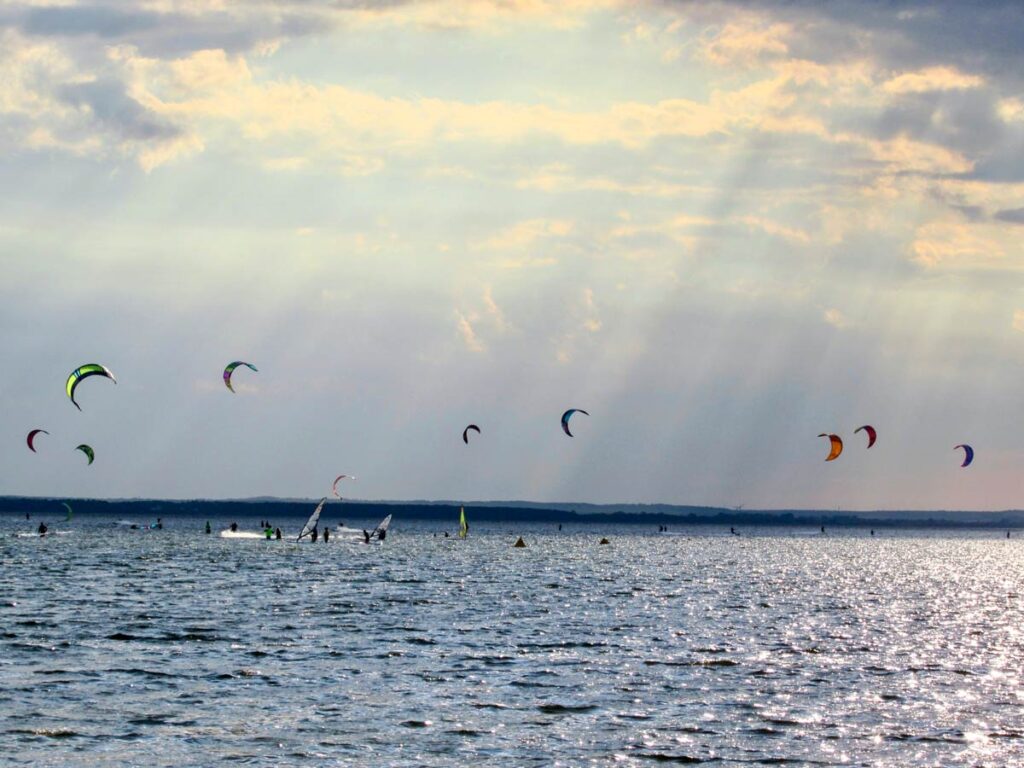 Surfer gleiten auf den Wellen der Halbinsel Hel, während der Wind über das kristallklare Wasser der Danziger Bucht fegt. Mit ihren farbenfrohen Surfbrettern genießen sie die idealen Bedingungen für Wind- und Kitesurfen, umgeben von der malerischen Küstenlandschaft.