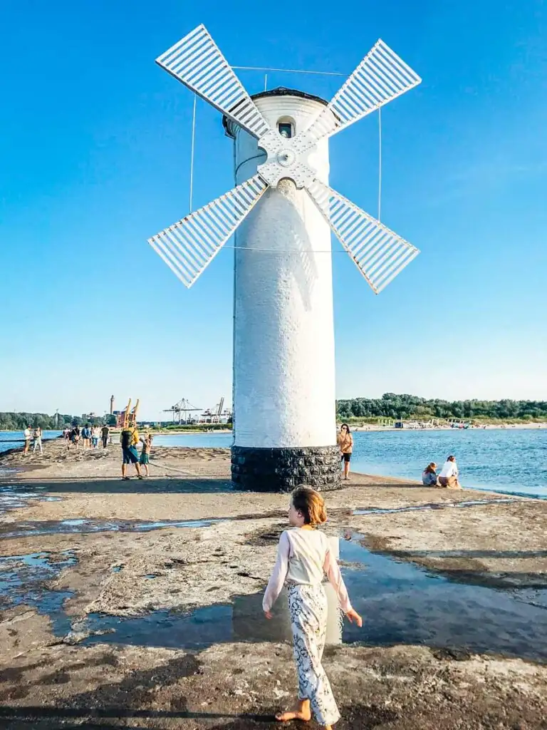 Blick von der Mühlenbake in Swinemünde in Richtung Land: Das historische Wahrzeichen an der Küste mit einem Blick auf den ruhigen Hafen und die umliegenden Kiefernwälder, die die Verbindung zwischen Meer und Stadt betonen.