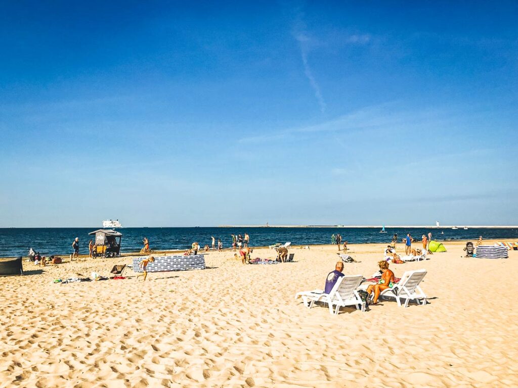 Sonnenbad am Strand von Swinemünde: Ein entspannter Tag am weiten Sandstrand, wo sich einige Menschen in der Sonne erholen. Im Hintergrund erstreckt sich die Polnische Ostsee, die mit ihrem klaren Wasser zur Abkühlung einlädt.