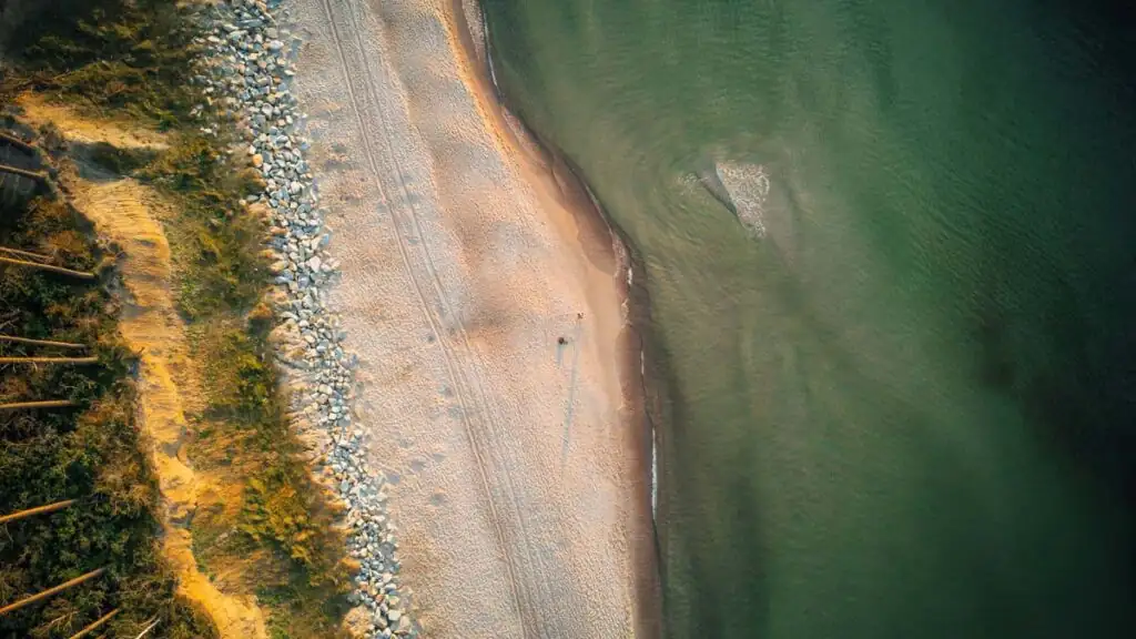 Drohnenaufnahme des Strands bei Rewal mit ruhiger Ostsee und weichem Sand, umgeben von grünen Dünen.