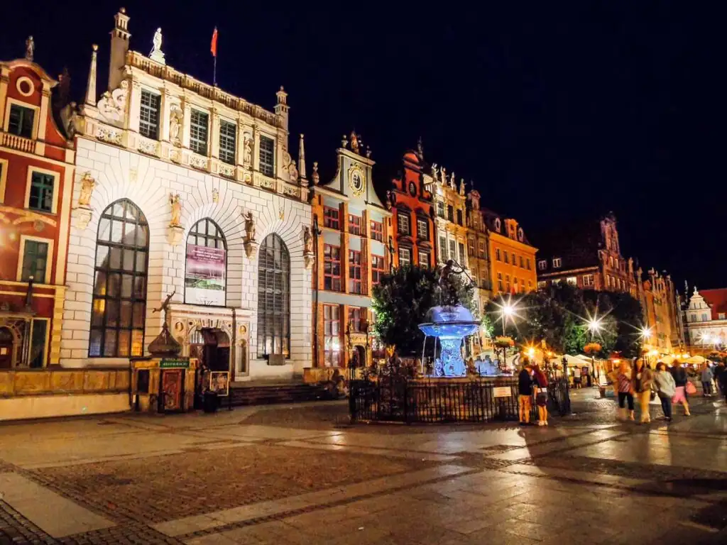 Beleuchteter Artushof und Neptunbrunnen bei Nacht am Langen Markt in Danzig.