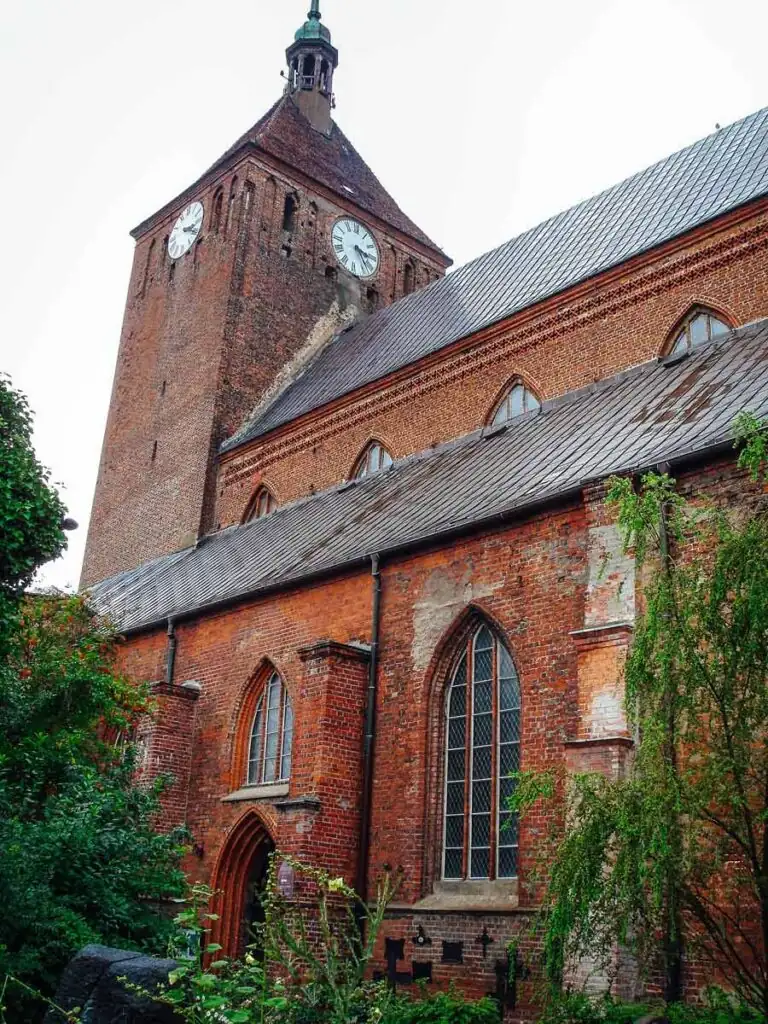 Außenansicht der Marienkirche in Darłowo mit ihrem hohen Turm und markanter Backsteinfassade.