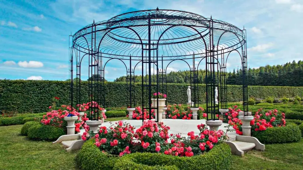 Pavillon in den Hortulus Themengärten bei Kolberg, umgeben von Blumen und Grünflächen.