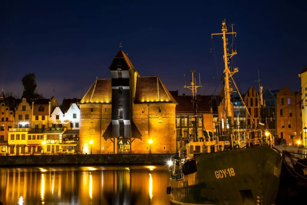 Das Krantor (Żuraw) in Danzig, bei Nacht beleuchtet, reflektiert im Wasser der Mottlau.