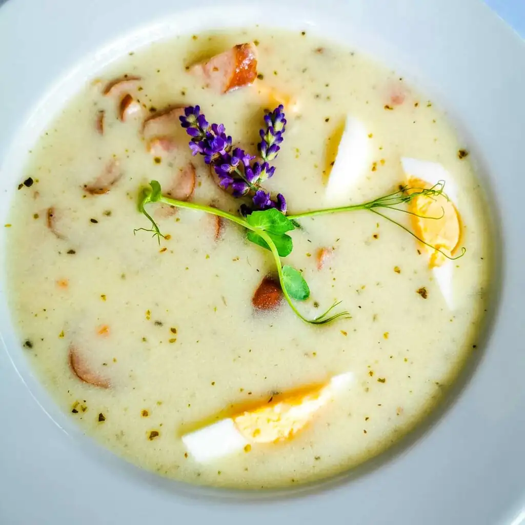 Polnische Suppe Żurek mit gekochtem Ei und Speck – traditionelles Gericht aus Sauerteigmehl