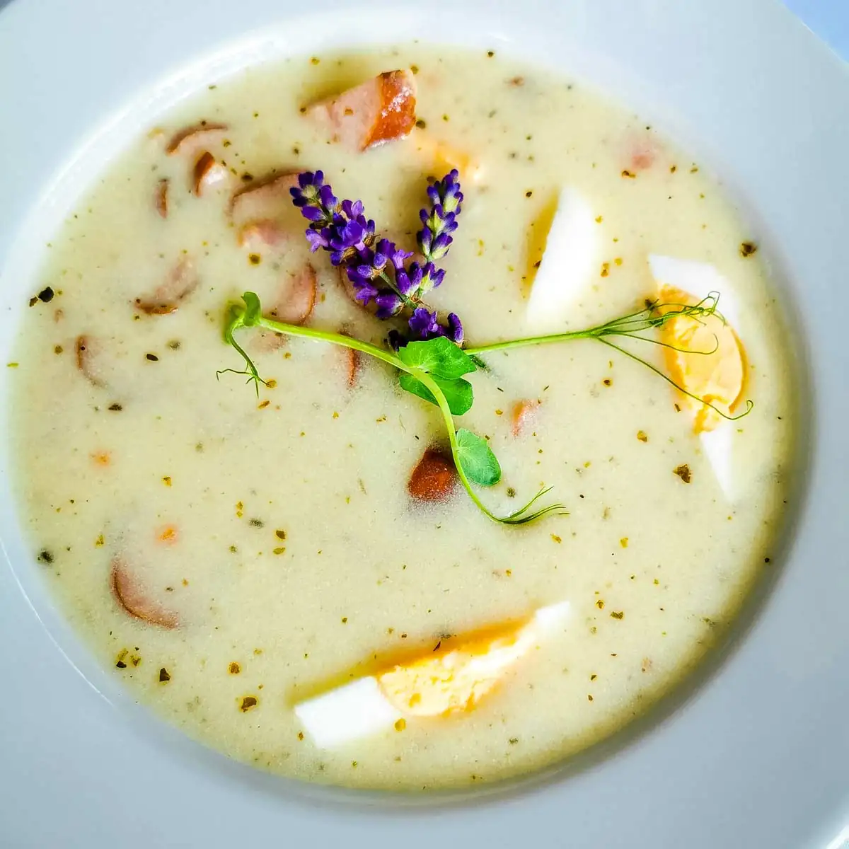 Polnische Suppe Żurek mit gekochtem Ei und Speck – traditionelles Gericht aus Sauerteigmehl