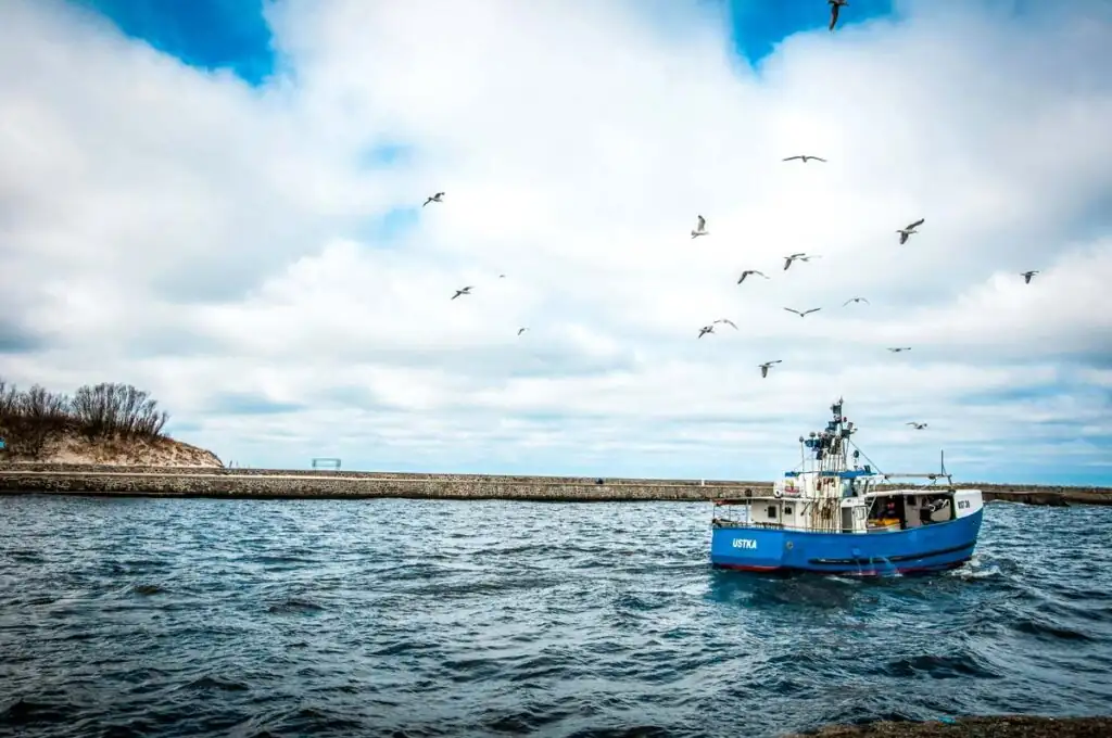Fischerboot bei der Ausfahrt aus dem Hafen von Ustka in Richtung Ostsee, Symbol für die lokale Fischereitradition und den Fischmarkt.