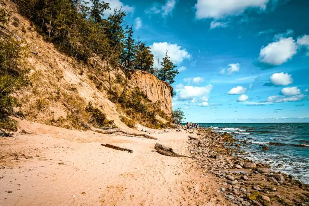 Strand bei Gdynia mit feinem Sand, sanften Wellen und bewaldeter Steilküste im Hintergrund
