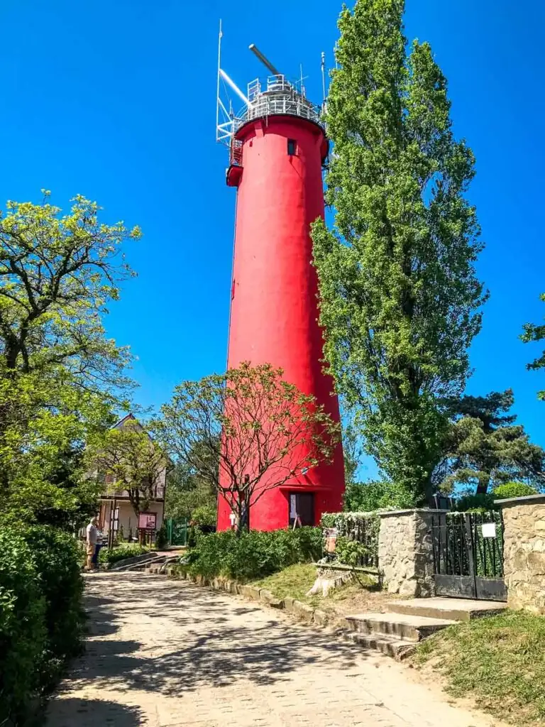 Roter Backstein-Leuchtturm von Krynica Morska, auf einer kleinen Düne am Wasser, unter blauem Himmel.
