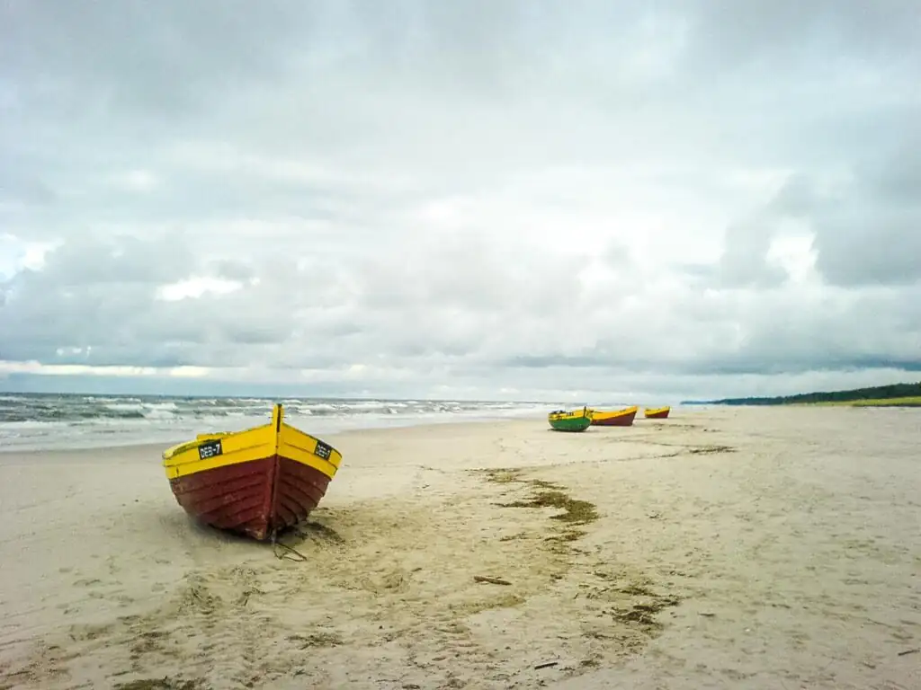 Mehrere kleine Fischerboote stehen auf dem breiten Sandstrand von Dębki vor der Ostsee.