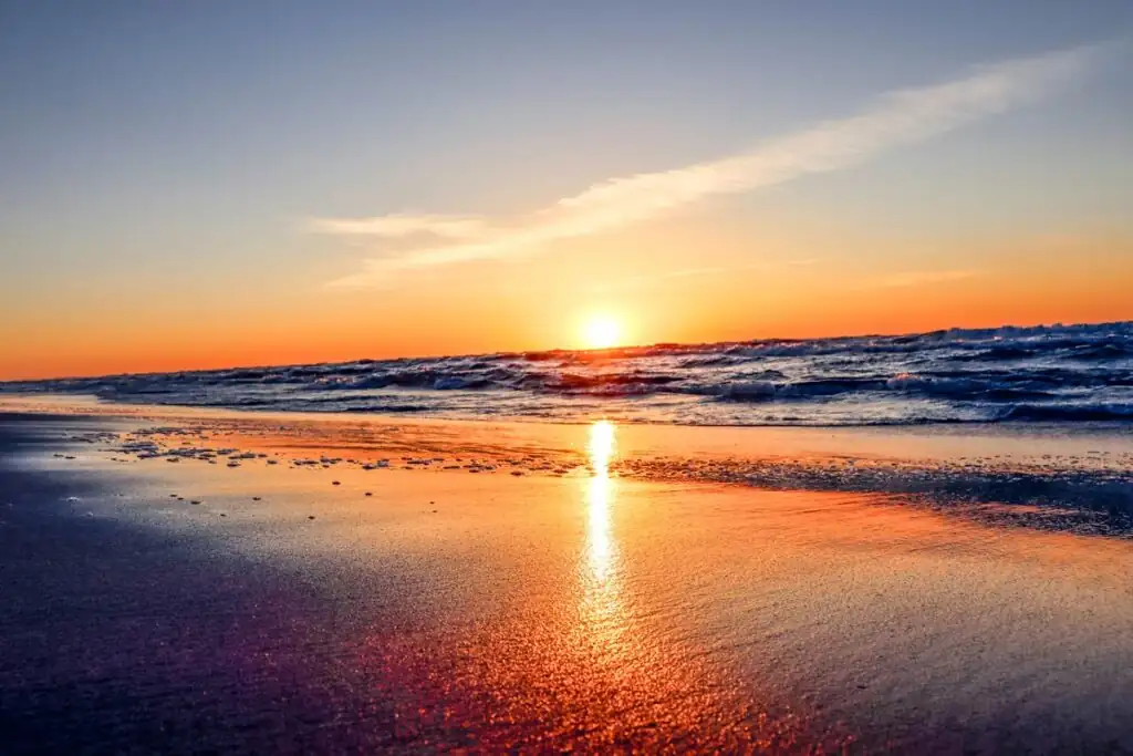 Tiefer Sonnenstand über der Ostsee, farbiger Himmel und nasser Sand am Strand von Dębki bei Sonnenuntergang.