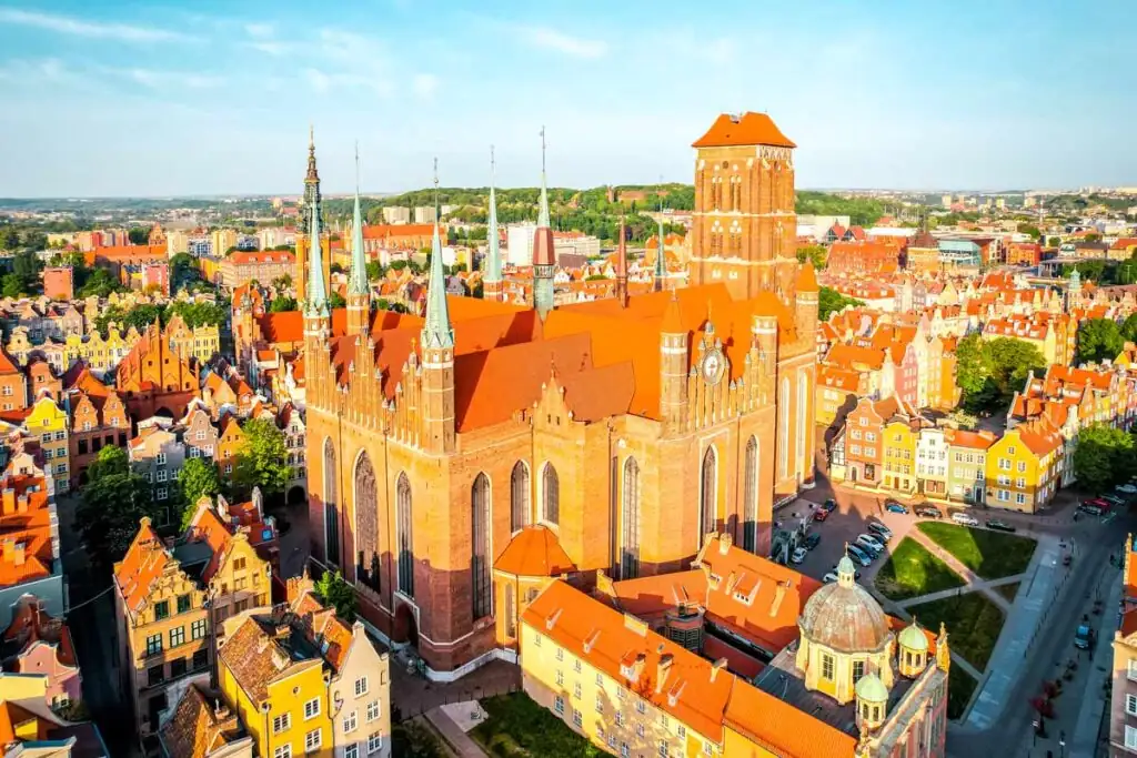 Luftaufnahme der Marienkirche (Bazylika Mariacka) in Danzig mit rotem Backsteindach, umgeben von den bunten Häusern der Altstadt.