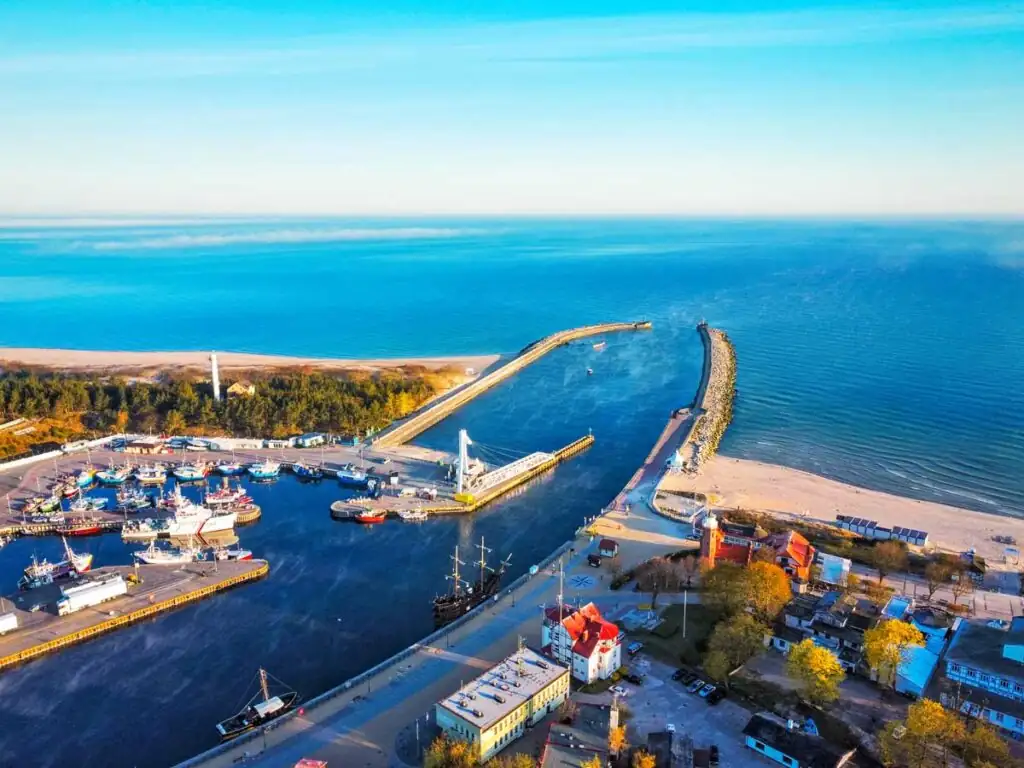 Drohnenaufnahme des Hafens von Ustka mit Leuchtturm, Klappbrücke, Fischerbooten und Blick auf die Ostsee.