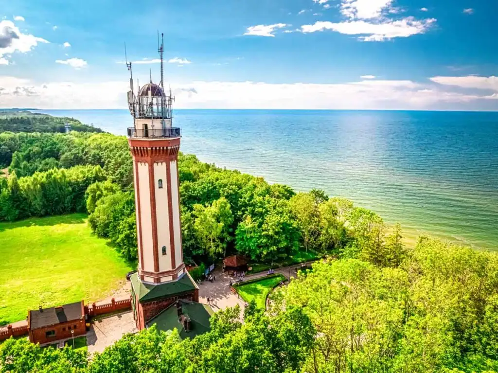 Luftaufnahme des Leuchtturms von Niechorze an der polnischen Ostsee, umgeben von Grünflächen und Küstenwald mit Blick aufs Meer.